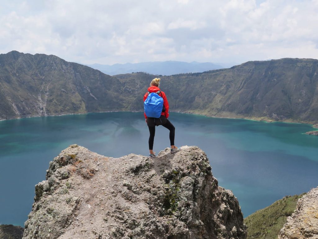 A woman stands on a rock looking over a lake