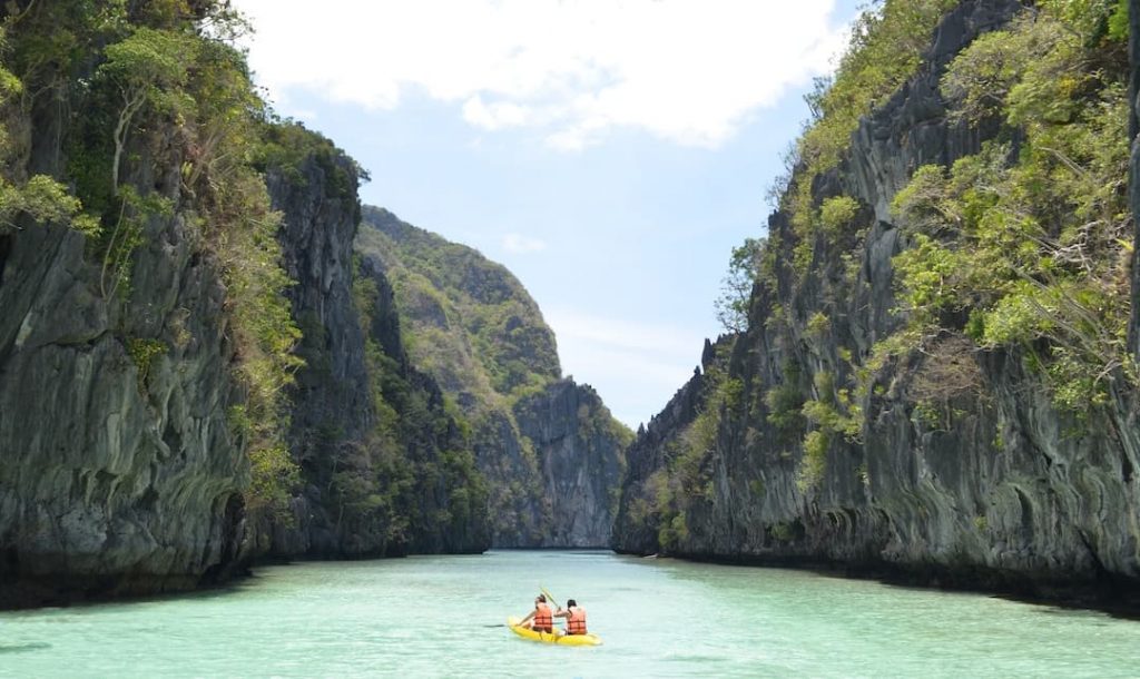 two people kayak through turquoise waters in the Philippines