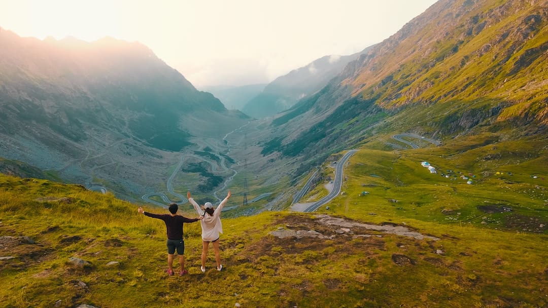 Two people standing with their arms up in the air overlooking a beautiful valley in Romania