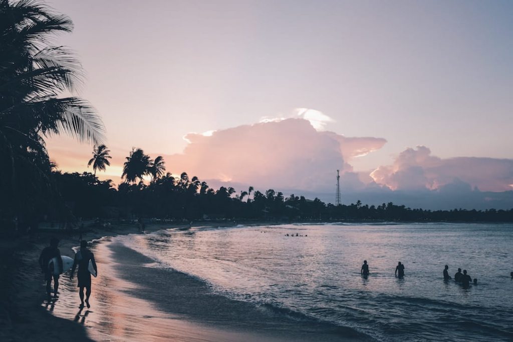 two surfers walk along a beach at dusk in Sri Lanka