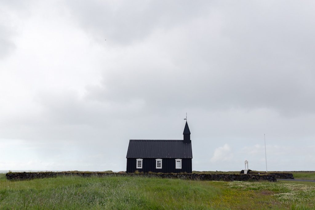 Black church with white windows sits in a grassy plain 