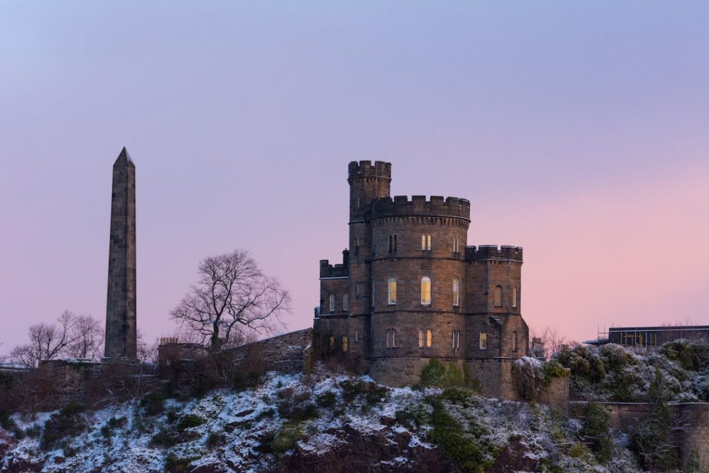 A Scottish castle with cylinder stone towers at dusk with patches of snow around it