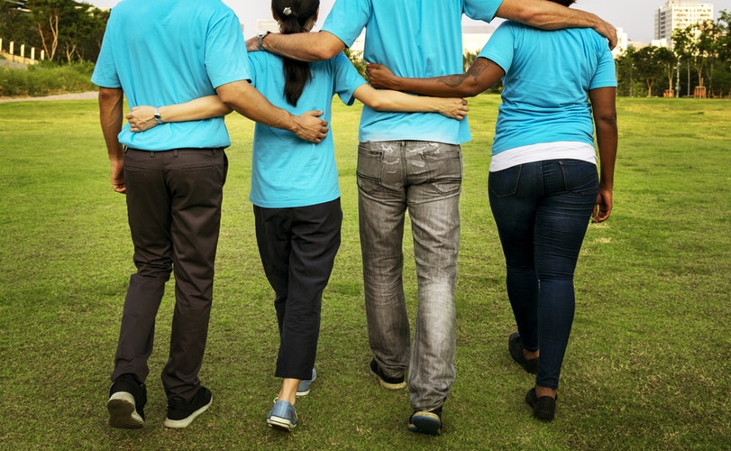 four people with matching blue shirts walking on green grass field