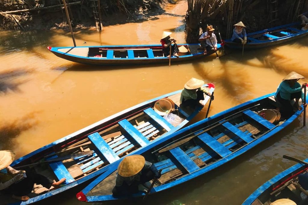 women in blue boats paddling along the Mekong River Delta in Vietnam