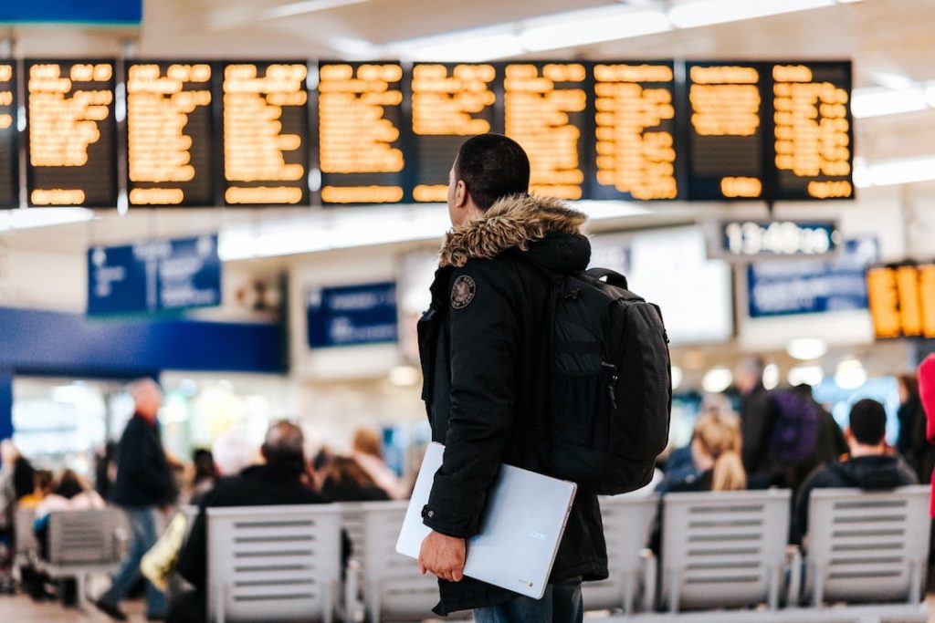 A man in a winter coat looks at an LED board of departure times in an airport