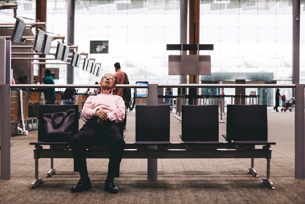 An older man in a pink shirt asleep on a set of gangchairs in an airport