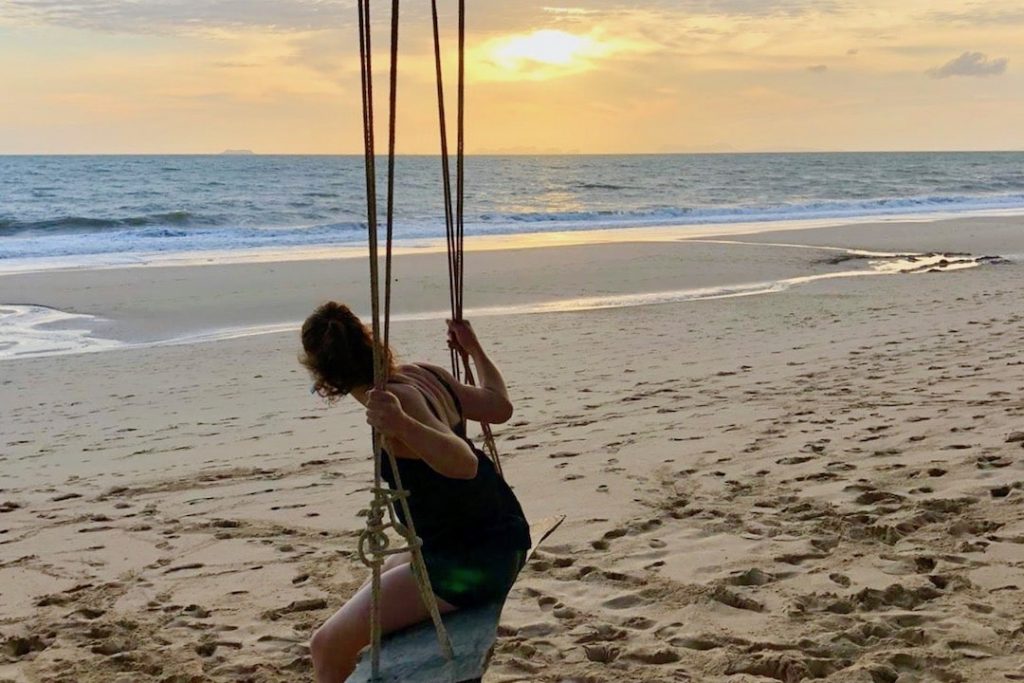 A girl sits on a swing on a beach looking out into the sea