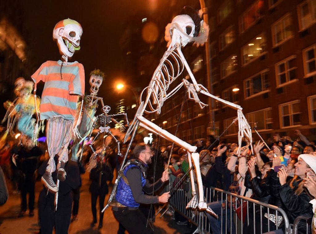 Street festival in NYC with large skeletons on stilts moving through the crowd 