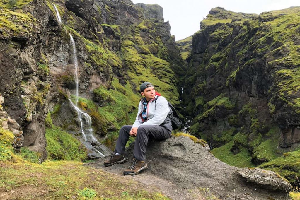 A man sits on a rock in front of a small waterfall in Southern Iceland