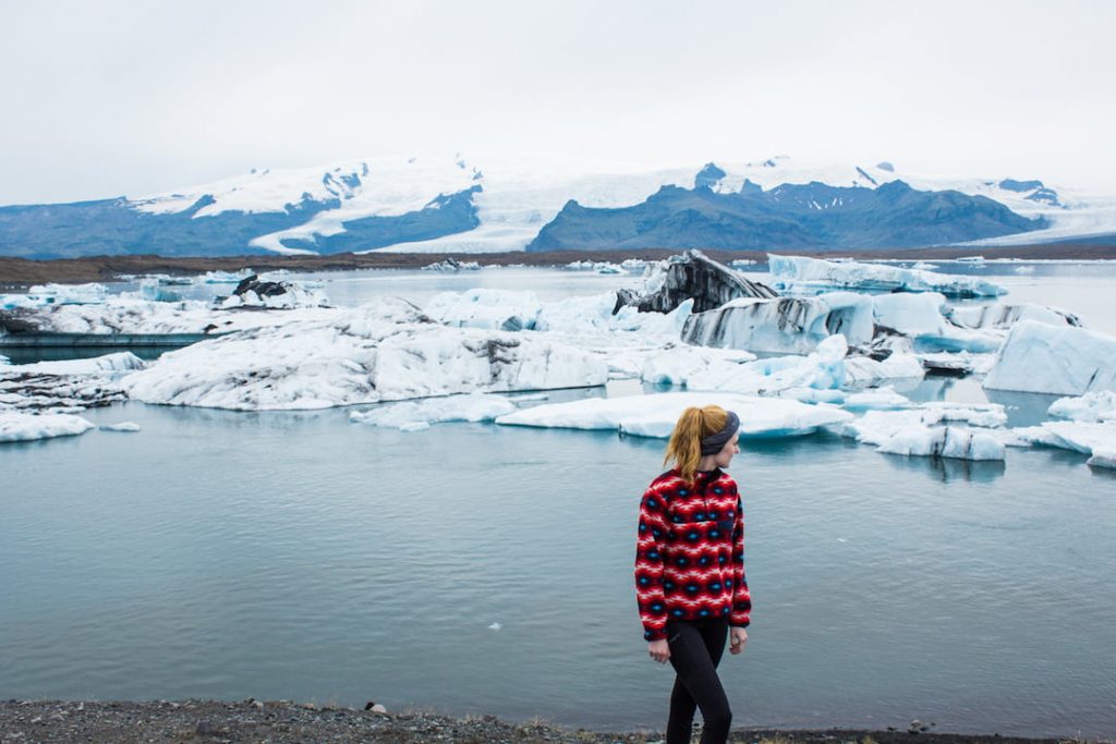 A girl faces away from the camera standing on a beach in Iceland