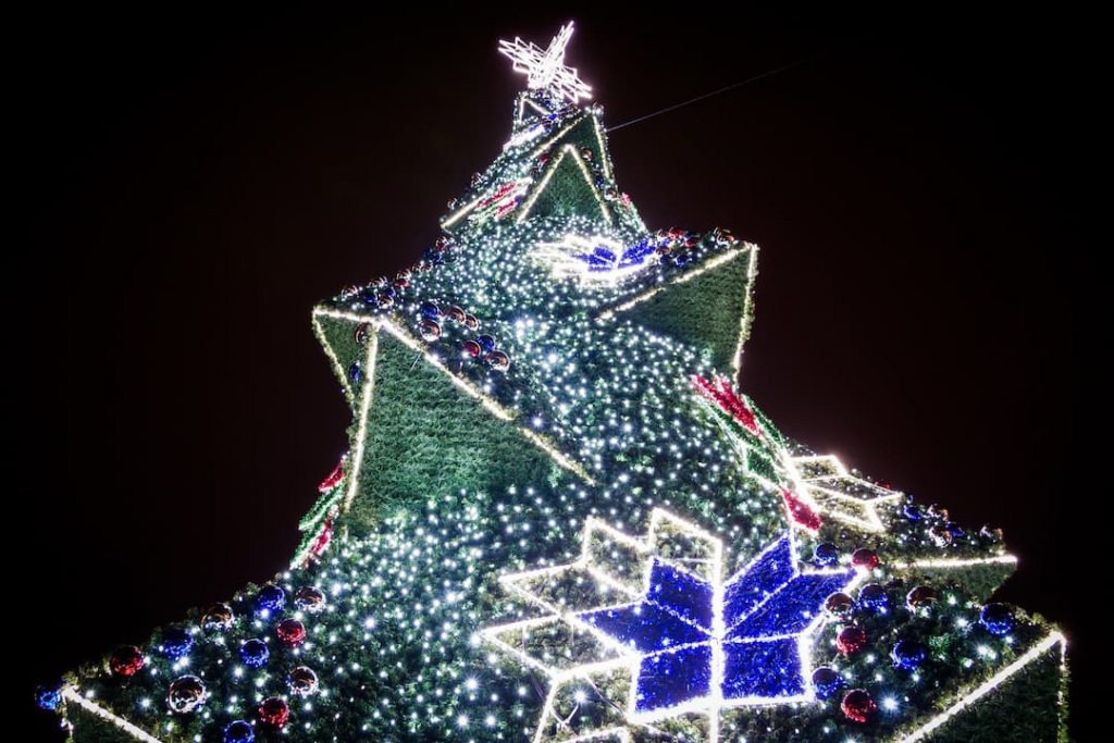 a green and blue christmas tree lit up by thousands of lights against the night sky