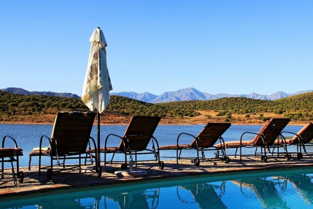 five deck chairs sitting by a pool with a body of water and mountain rage in the background in Klein Karoo, South Africa