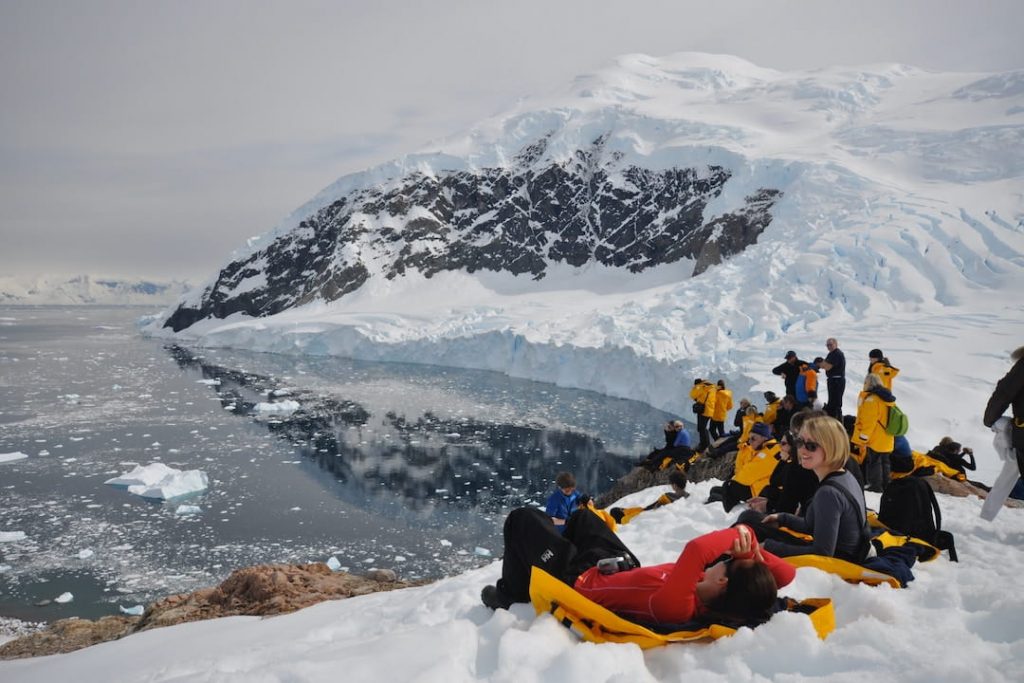 A group of people in cold-weather coats relaxing on the bank of a glacier in Antarctica