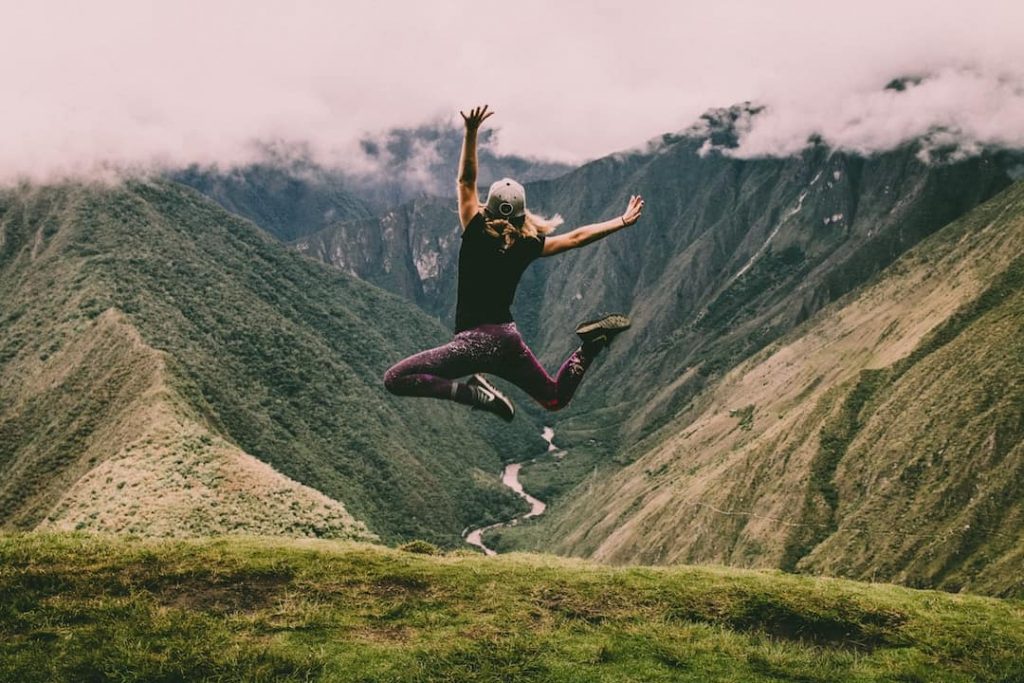 A woman with her back to the camera jumps in the air at Machu Picchu, Peru