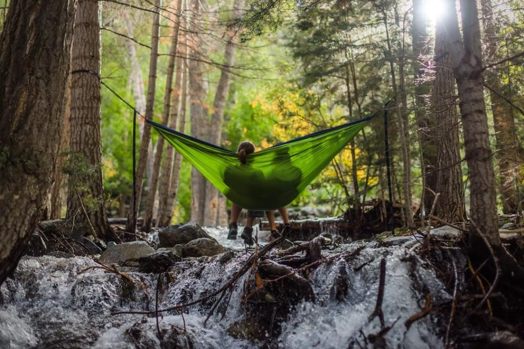 Two people sitting in a green hammock over a river