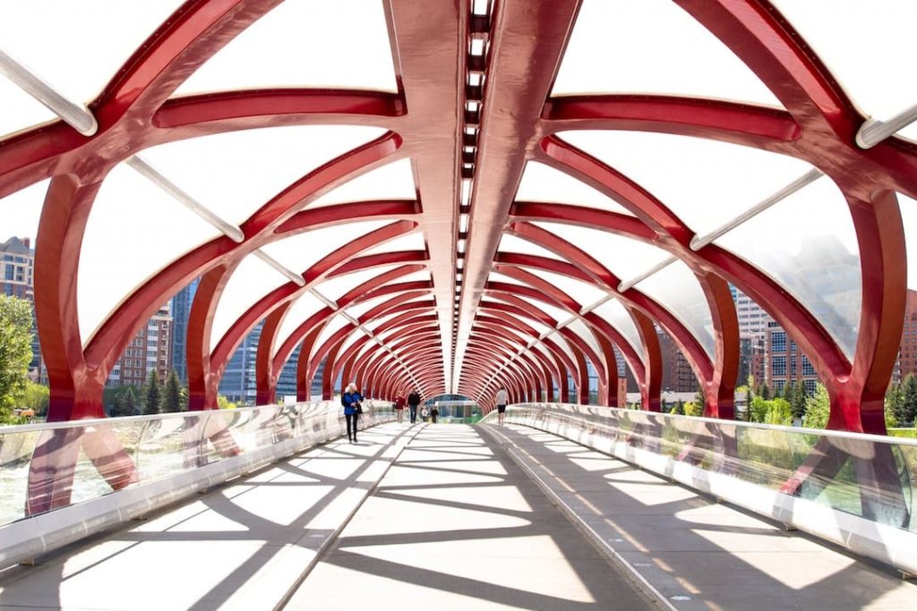 People walking on a large red geometric bridge in Calgary, Alberta