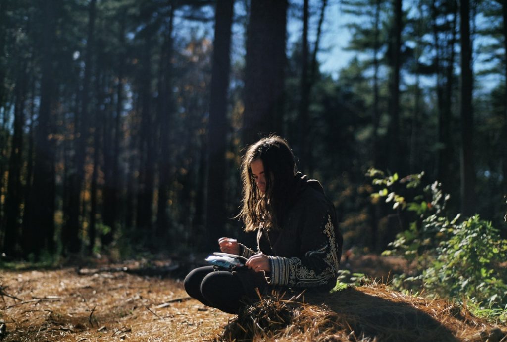 woman wearing black and gray top sitting during daytime scribbling in her book