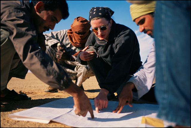 a woman and three guides look at a map in desert surroundings