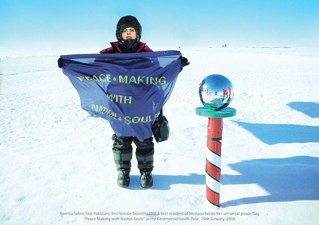 a women in a snow suit holds up a flag beside the south pole