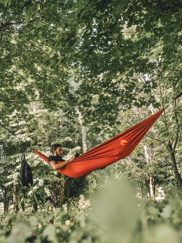 man on red hammock surrounded by trees during daytime