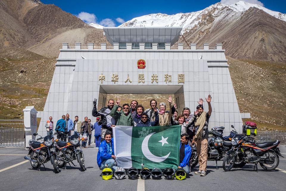 a group of people stand in front of an arch holding a green and white flag waving at the camera