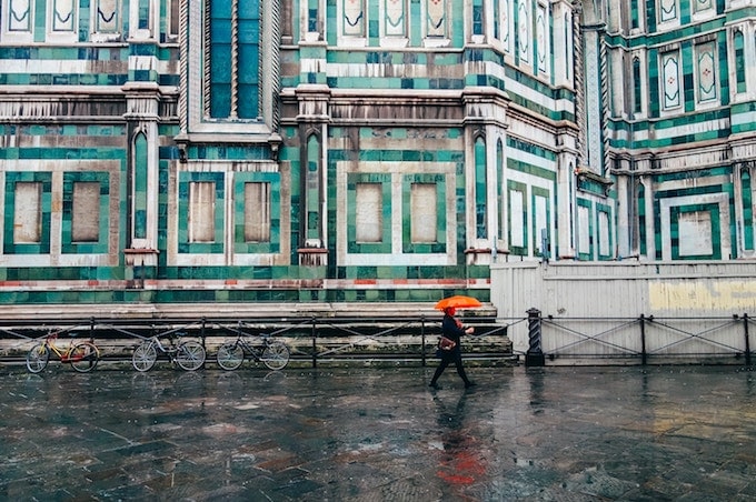 A person with an orange umbrella in front of a blue building in Florence, Italy