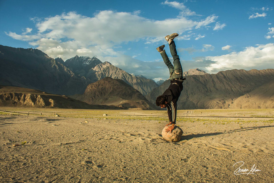 A man doing a handstand on the rocks with the mountains in the background in the north of Pakistan