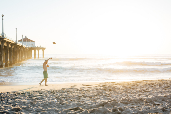 a man walking a beach throwing the ball in the air