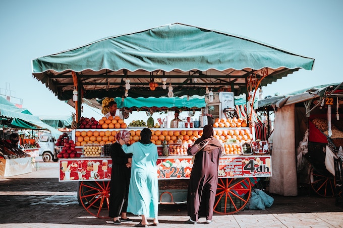 Women in front of a fruit stand in a market in Marrakesh, Morocco