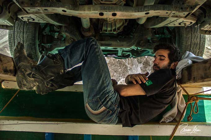 a man relaxing under a truck, looking very cool, with a pakistani flag on his t-shirt