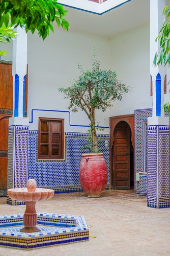 a colourful riad with tile work, plants and a small arabic fountain