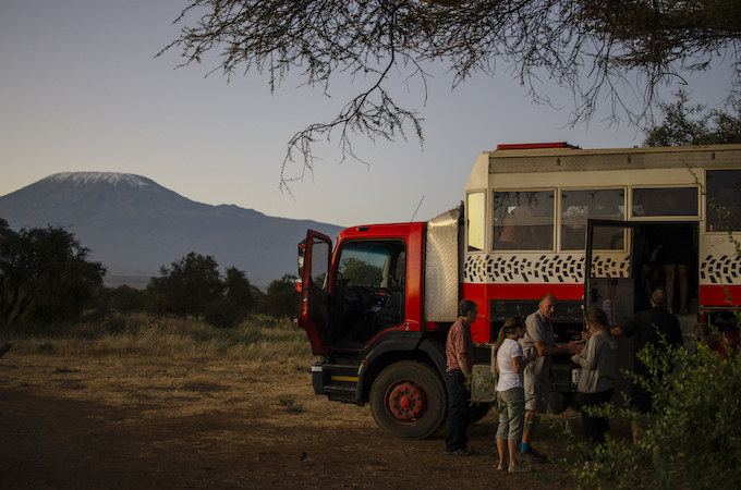 a large orange truck is in the forefront of a landscape with a beautiful solo mountain in the background