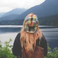 A woman in a colourful hat stands facing a lake in British Columbia