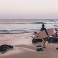 A person carrying a surfboard by Byron Bay