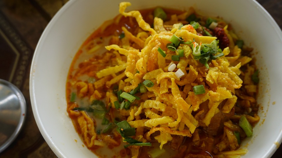 a bowl of a red coloured broth topped with crispy noodles and vegetables