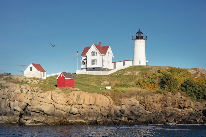 A white and red lighthouse on the water in Maine