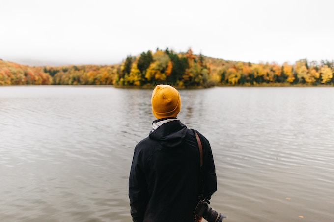 A person in a gold winter hat standing in front of fall foliage in Vermont