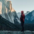 A person in a red coat standing by El Capitan in Yosemite National Park, California