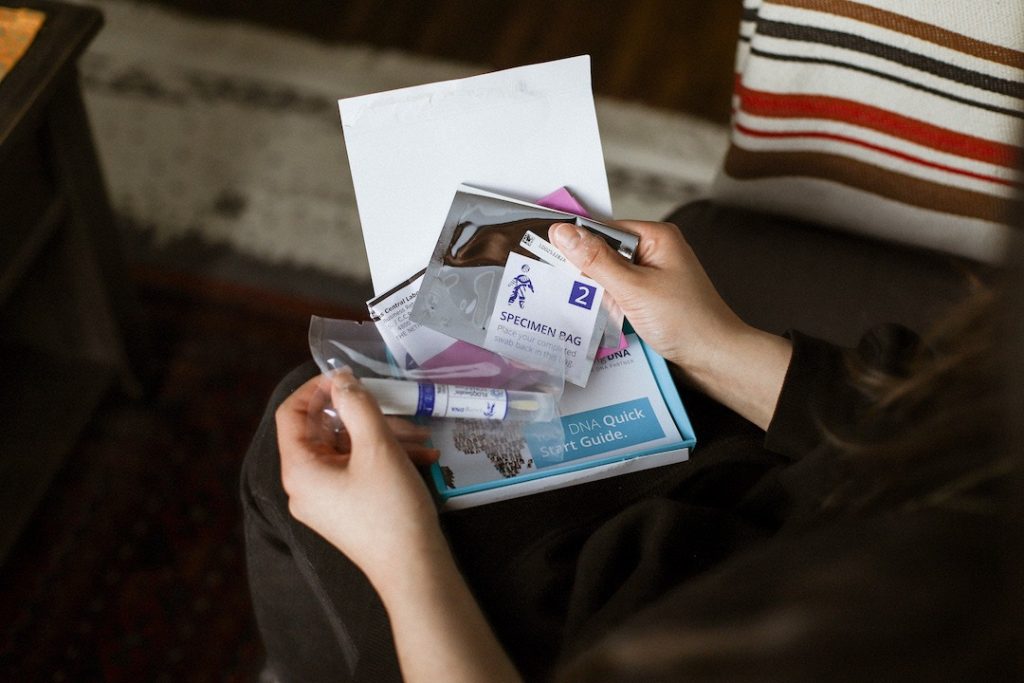 hands holding a small white and blue box which has a DNA sampling kit in it