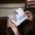 hands holding a small white and blue box which has a DNA sampling kit in it