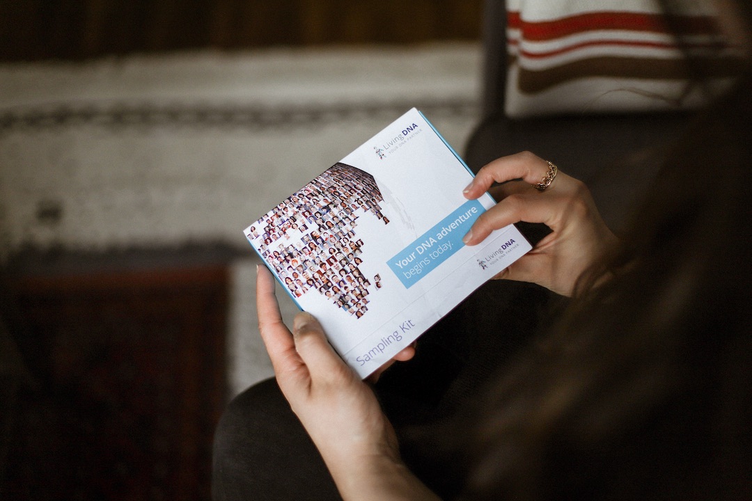 hands holding a small white and blue box which has a DNA sampling kit in it