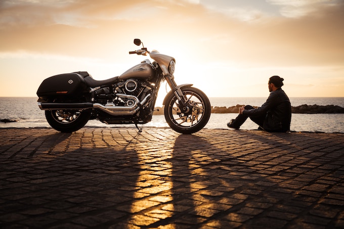 A man sitting beside a motorcycle at sunset