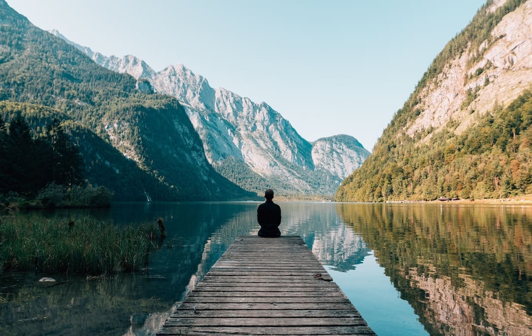 A man sitting on the edge of a dock facing a mountain in Germany