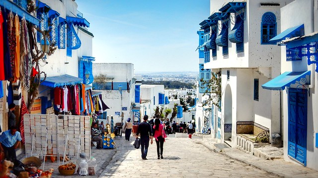 two people walking along a road with blue and white buildings