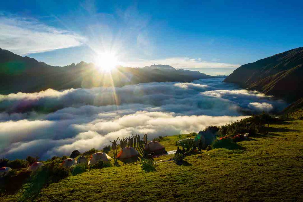 a long distance shot a people on the mountains with tents looking out at the clouds