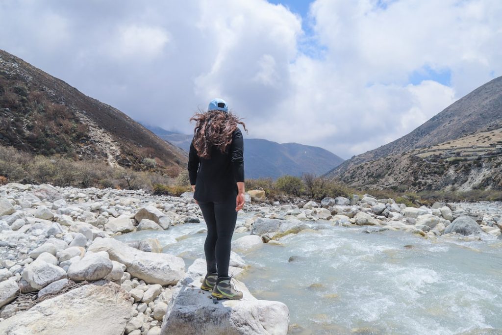 a girl in a blue cap standing on rocks in the rive