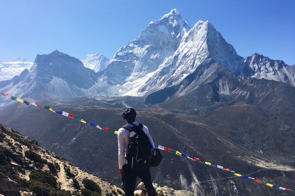 climber with a backpack stands in front of mountain peaks with colourful flags