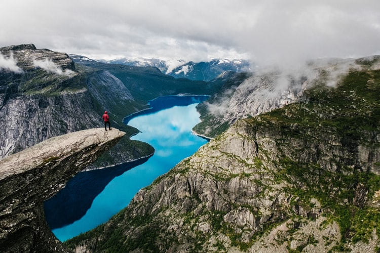 man standing on a thin sliver of protuding rock over a valley