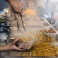 steam coming off piles of noodles as a street vendor serves them up