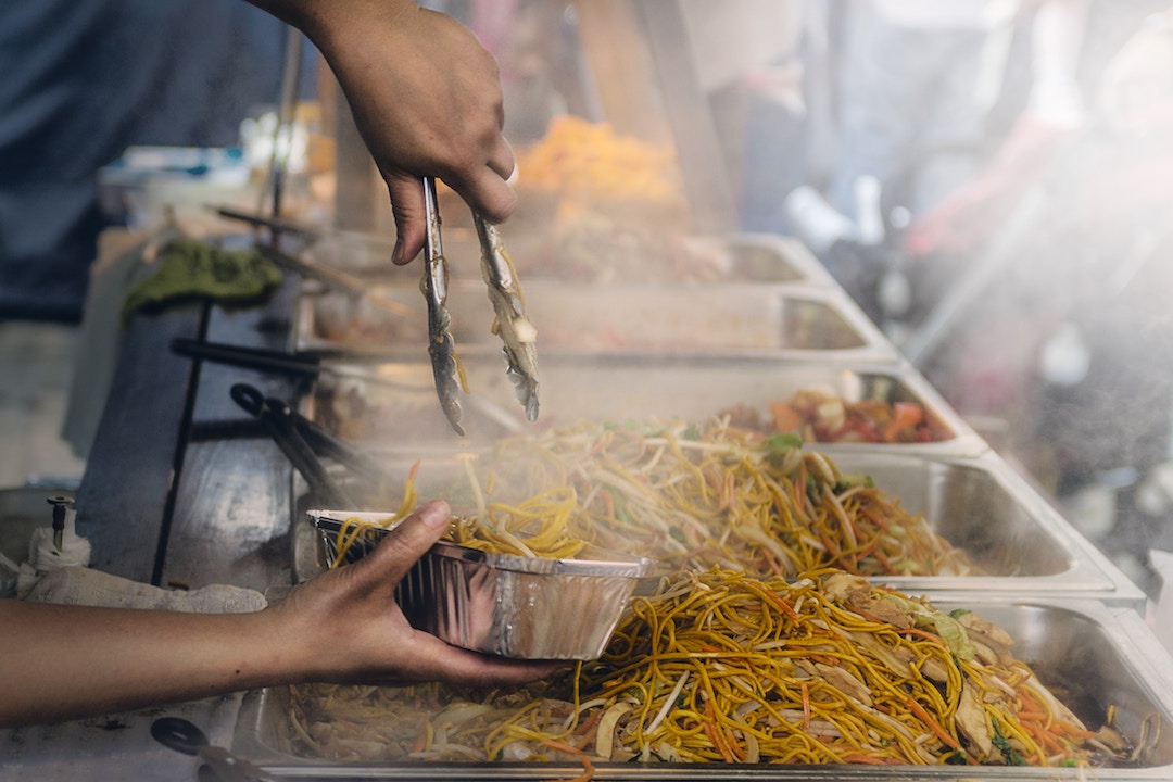 steam coming off piles of noodles as a street vendor serves them up